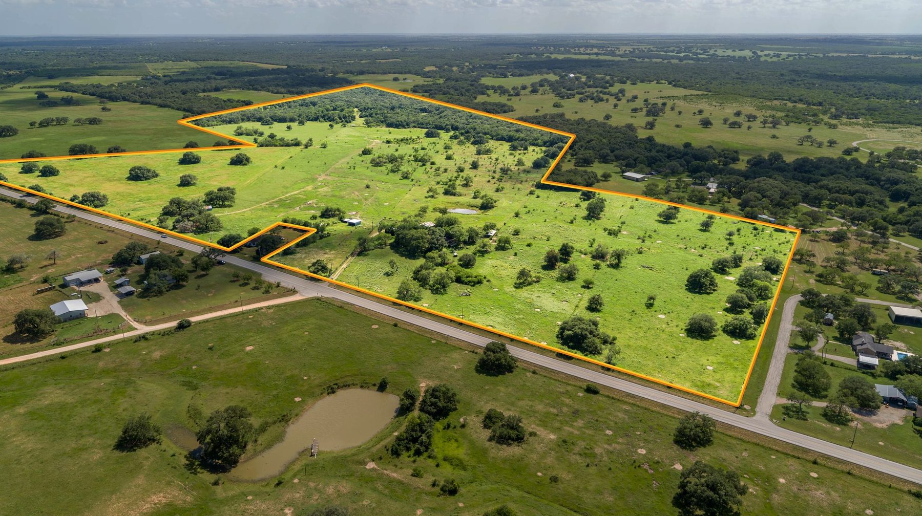 Aerial property-boundary overlay — green pasture parcel with road frontage and pond, drawn over an orthographic drone aerial by Aerialcam Media